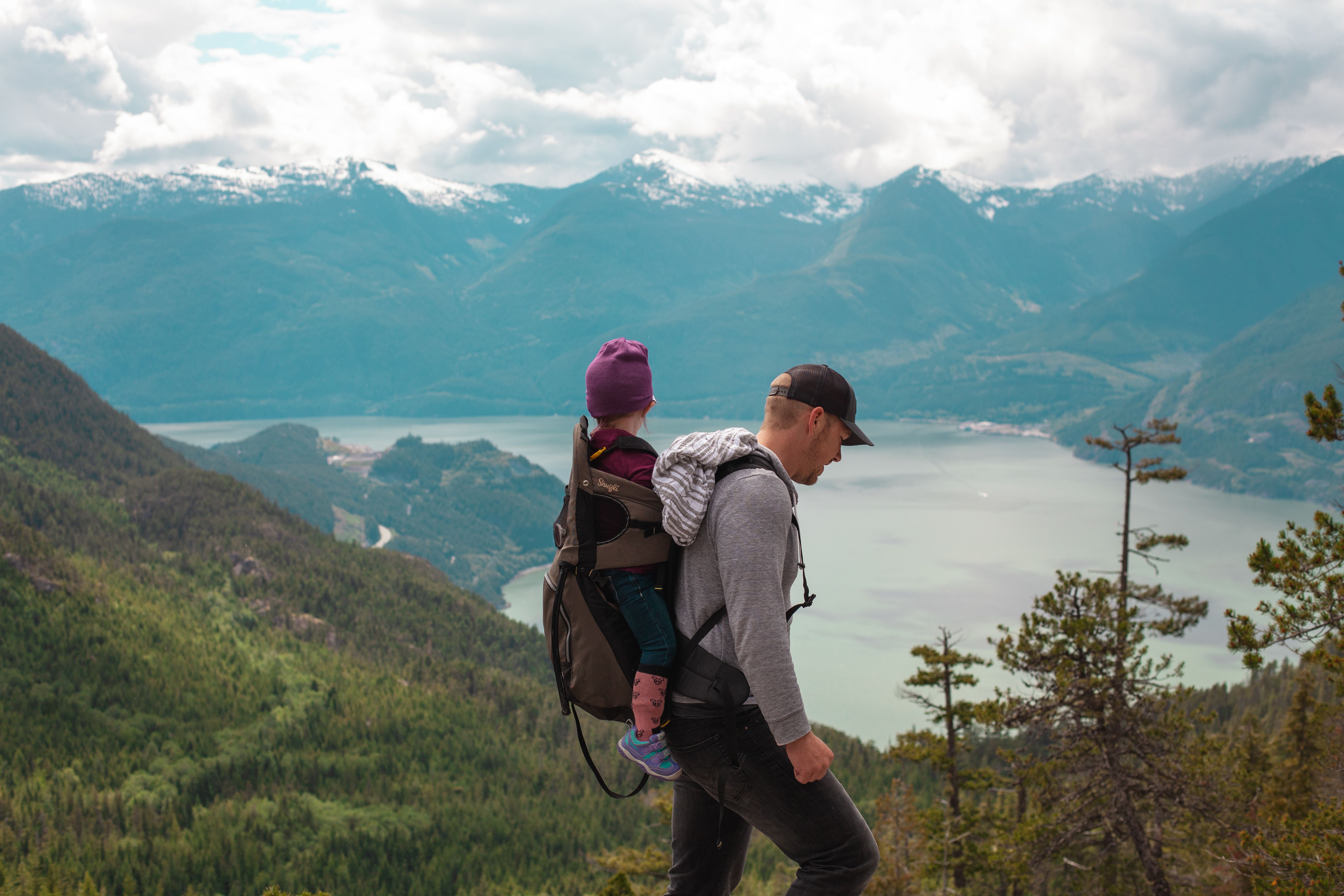 A parent hiking with a child in a backpack carrier above a mountain lake